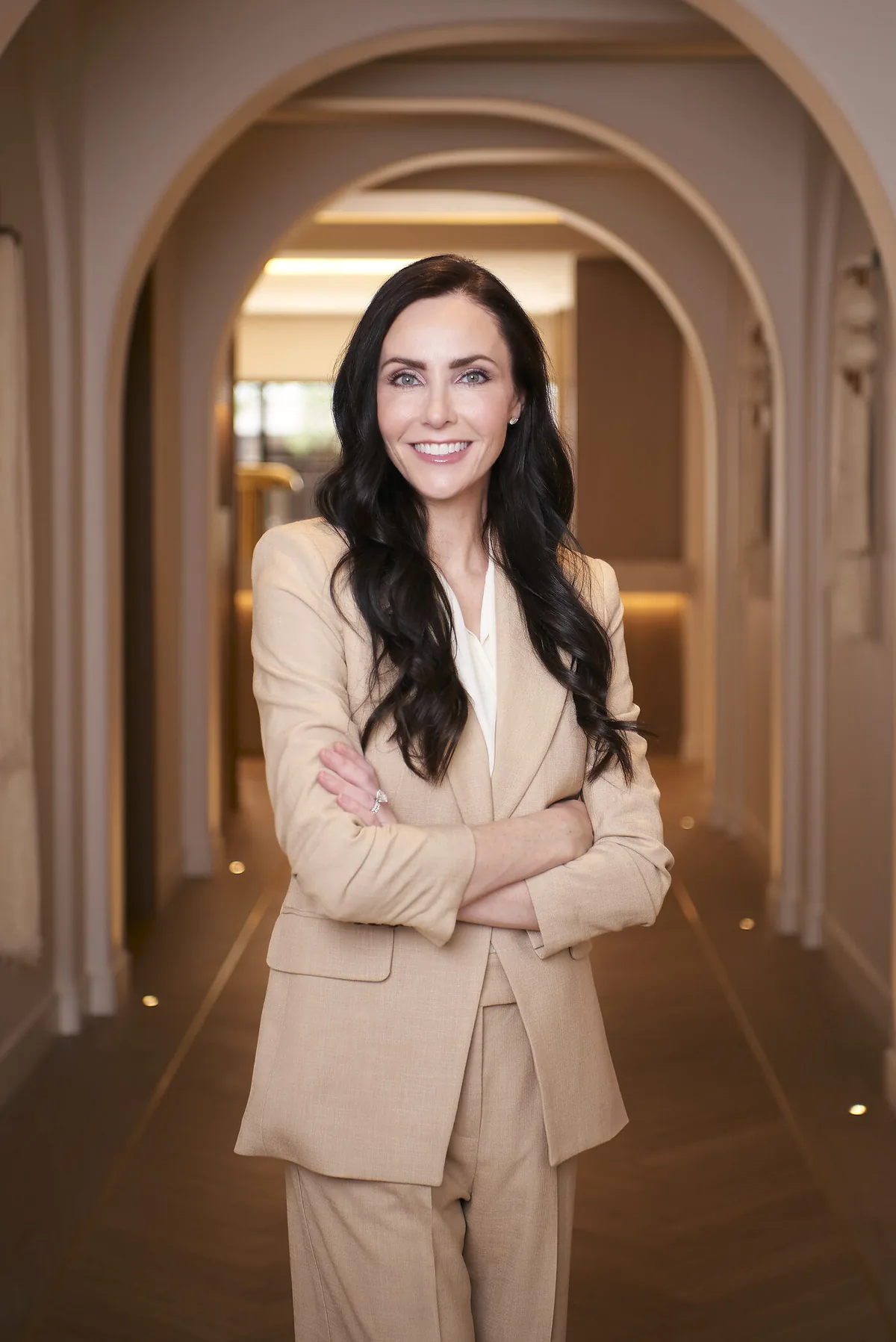 Dr. Ashley Howarth in a tan suit in the arched white-oak corridor of her Scottsdale practice